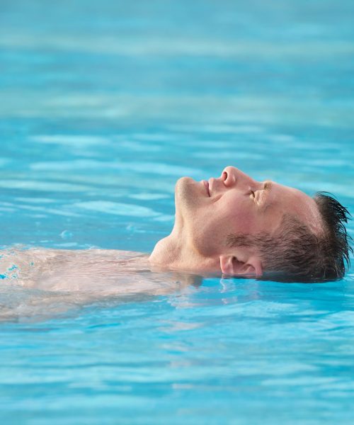 head of relaxed man keeping his eyes closed while taking pleasure in warm water